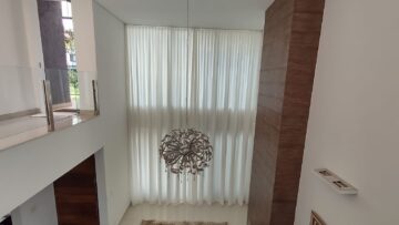 Cortina translúcida em sala com pé-direito duplo: a automação permite controlar a entrada de luz com um comando.